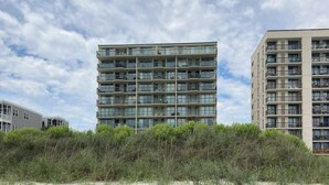 A multi-story residential building with balconies, situated next to a sandy beach with dense vegetation. - Endless Summer Oasis (North Myrtle Beach)