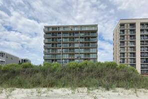 Ein mehrstöckiges Wohngebäude mit Balkonen, direkt neben einem Sandstrand mit dichter Vegetation.
