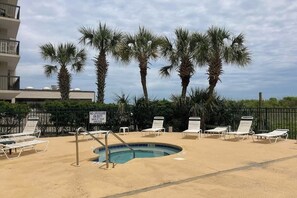 Un espace piscine aménagé avec des chaises longues, des palmiers et un panneau indiquant qu’il n’y a pas de sauveteur de service.