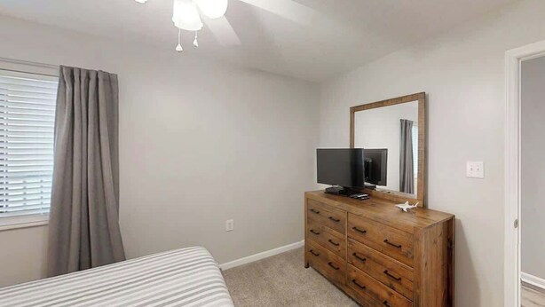 A bedroom with a bed, a wooden dresser, a television, and a ceiling fan. - Endless Summer Oasis (North Myrtle Beach)