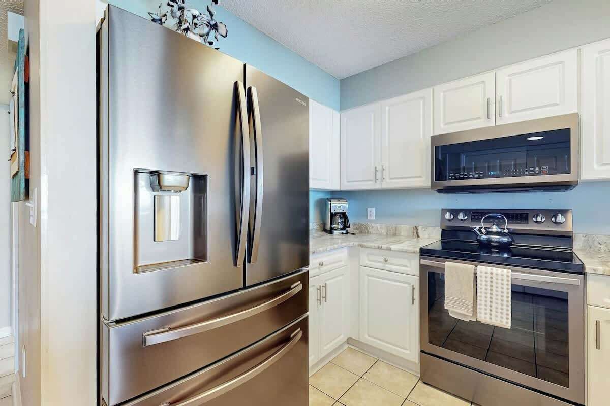 Una cocina con electrodomésticos de acero inoxidable, gabinetes blancos y piso de baldosas.