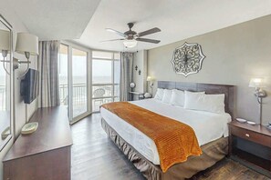 A hotel room with a large bed, a ceiling fan, a balcony with curtains, and a decorative wall piece. - Sunrise Tides at the Cherry Grove Pier (North Myrtle Beach)