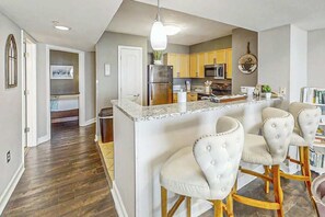 A modern kitchen with a central island, bar stools, and a dining area. - Sunrise Tides at the Cherry Grove Pier (North Myrtle Beach)