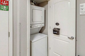 A laundry room with a washing machine, a dryer, and a door with a temperature control sign. - Sunrise Tides at the Cherry Grove Pier (North Myrtle Beach)