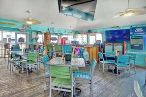Un restaurant aux murs de couleur turquoise, aux chaises vertes et au plancher en bois. On y trouve des tables, des chaises et un comptoir avec un menu.