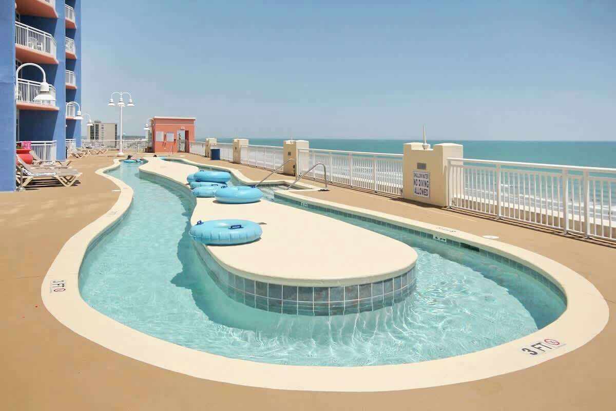A pool area with a hot tub, lounge chairs, and a view of the ocean.