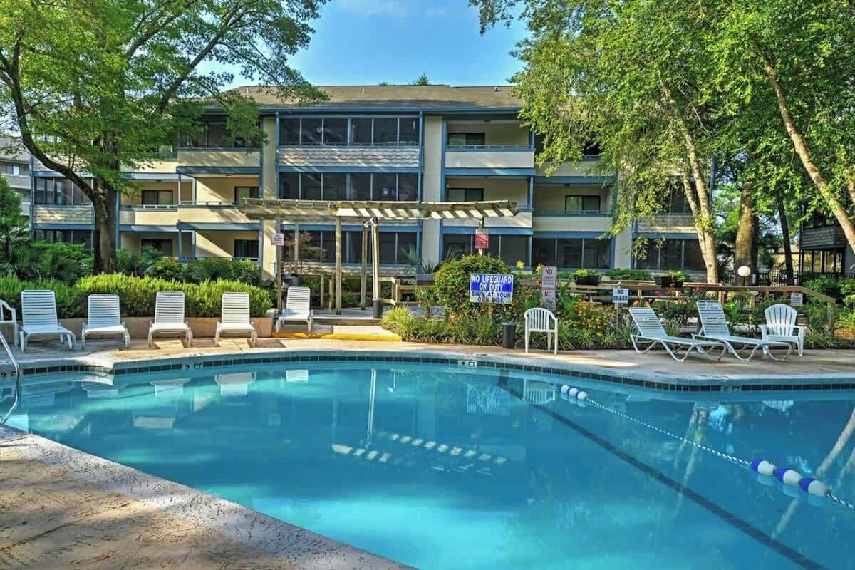 A swimming pool with lounge chairs and a building with multiple balconies in the background.