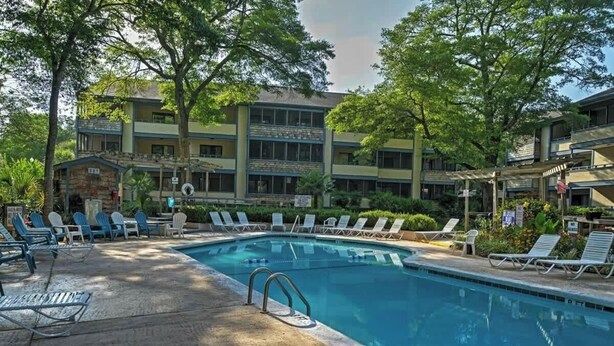 Una piscina con lettini e un edificio a più piani con balconi.