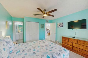 Une chambre à coucher avec un lit, un ventilateur de plafond, une commode et un téléviseur fixé au mur.