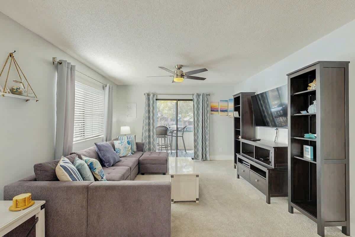 Ein Wohnzimmer mit Ecksofa, Flachbildfernseher, Deckenventilator und Bücherregal.