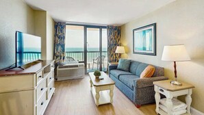 A living room with a television, a sofa, a coffee table, and a lamp. There is a balcony with a view. - Oceanfront Paradise Retreat (Myrtle Beach)