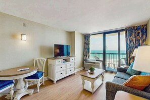 Ein Hotelzimmer mit Balkon, Fernseher, Esstisch, Sofa und Kommode.