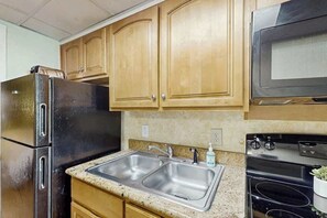 Eine Küche mit Holzschränken, einem Edelstahlkühlschrank, einer Spüle mit zwei Becken und einer schwarzen Mikrowelle.