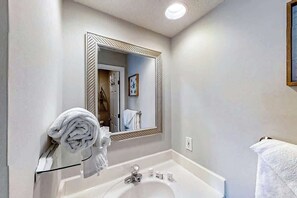 Ein Badezimmer mit weißem Waschbecken, einem Spiegel mit dekorativem Rahmen und einem Handtuchhalter mit gefalteten Handtüchern.