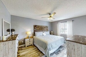 Ein Schlafzimmer mit einem Bett, Nachttischen, einem Deckenventilator, einem Fenster mit Vorhängen und einem Holz-Kopfteil.