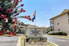 Schild für das Tilghman Shores Ocean & Golf Resort mit einer Flagge, umgeben von Gebäuden und einem klaren Himmel.