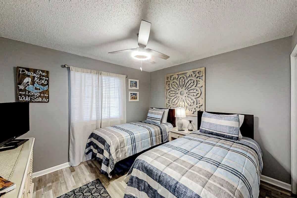 Ein Schlafzimmer mit zwei Betten, einem Deckenventilator, einem Fenster mit Vorhängen und Wandbildern.