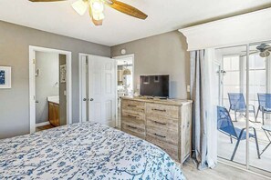 A bedroom with a bed, a dresser, a television, and a sliding glass door leading to a balcony with chairs. - Waterway Landing 216-A (North Myrtle Beach)