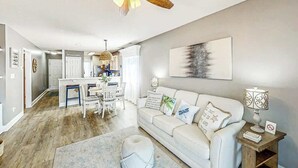 Ein modernes Wohnzimmer mit einem weißen Sofa, einem runden Hocker und einem Essbereich mit einem weißen Tisch und Stühlen.