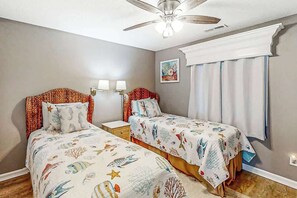 Une chambre avec deux lits, un ventilateur de plafond et une fenêtre avec des rideaux.