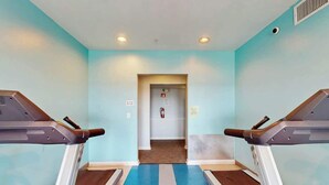 Ein Fitnessraum mit Laufbändern, einem blau-weißen Boden und einer Tür zu einem weiteren Raum.