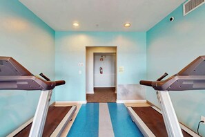 Ein Fitnessraum mit Laufbändern, einem blau-weißen Boden und einer Tür zu einem weiteren Raum.