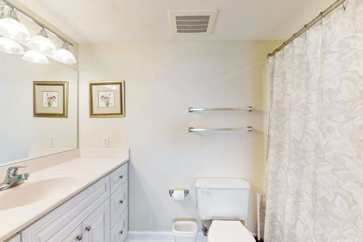 Een badkamer met een wit wastafelmeubel, een spiegel, een toilet, een douchegordijn en een handdoekhouder.