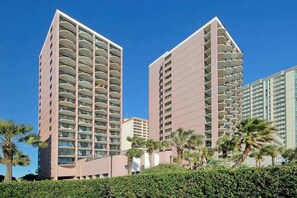 A high-rise hotel with multiple balconies, surrounded by palm trees and a clear sky. - Coastal Living Retreat (Myrtle Beach)