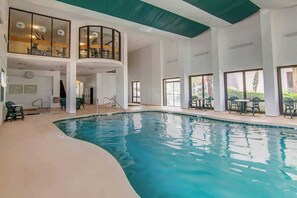 En indendørs swimmingpool med buet kant, omgivet af siddeområder og store vinduer.
