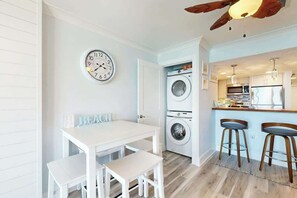 A compact kitchen with a washing machine, a dining area with a table and chairs, and a ceiling fan. - Coastal Living Retreat (Myrtle Beach)