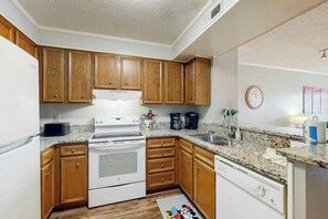 Une cuisine de taille réduite, dotée de meubles en bois, d’un réfrigérateur blanc, d’une cuisinière et d’un lave-vaisselle.