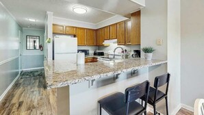 Eine moderne Küche mit Granit-Arbeitsplatten, Holzschränken und einer integrierten Kücheninsel mit Barhockern.