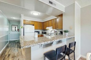 A modern kitchen with granite countertops, wooden cabinets, and a built-in island with bar seating. - Tilghman Beach & Racquet 259 (North Myrtle Beach)