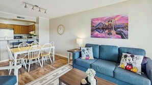 Ein modernes Wohnzimmer mit einem blauen Sofa, einem Esstisch und Stühlen. An der Wand hängt ein Bild von einem Riesenrad.