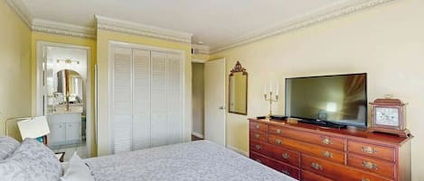 Una camera d'albergo con un letto, una cassettiera, una televisione e uno specchio.