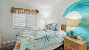 Ein Schlafzimmer mit einem Bett, einem Nachttisch, einer Lampe, einem Fenster mit Jalousien und einer Wand mit einem großen Gemälde.
