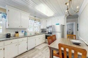 A modern kitchen with white cabinetry, a dining table, and a chandelier. - Sea Breeze Beach Retreat (North Myrtle Beach)