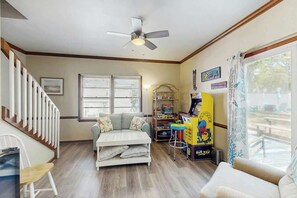 Ein Wohnzimmer mit Sofa, Couchtisch, Bücherregal, Deckenventilator und einem Fenster mit Jalousien.
