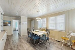 A dining area with a table and chairs, a kitchen area with cabinets, and a hallway leading to another room. - Sea Breeze Beach Retreat (North Myrtle Beach)