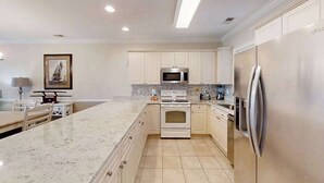 A modern kitchen with white cabinetry, a central island, stainless steel appliances, and a tiled floor. - Luster Leaf Unit 303 (Myrtle Beach)