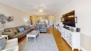 A modern living room with a sofa, coffee table, and a TV on a white cabinet. - Luster Leaf Unit 303 (Myrtle Beach)