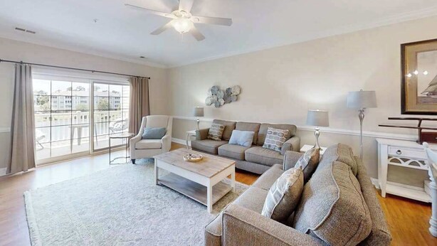 A spacious living room with a ceiling fan, a sofa set, a coffee table, and a view through large windows. - Luster Leaf Unit 303 (Myrtle Beach)