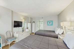 A hotel room with two beds, a TV, a desk, a chair, and a bathroom door. - Sandcastle South 1102 (Myrtle Beach)