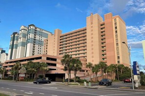 A multi-story hotel with a parking garage and palm trees in front. - Sandcastle South 1102 (Myrtle Beach)