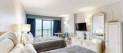 A hotel room with two beds, a TV, a desk, and a balcony with a view.