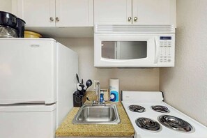 A compact kitchenette with a white refrigerator, a microwave, a sink with a faucet, and a stove with four burners. - Sandcastle South 1102 (Myrtle Beach)