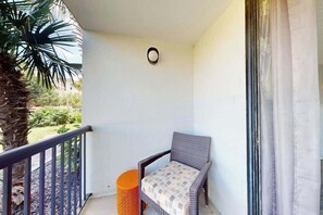 Ein Balkon mit einem Korbstuhl, einem kleinen orangefarbenen Hocker und einer Palme.