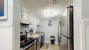 A compact kitchen with white cabinetry, stainless steel appliances, and a tiled backsplash. - Holiday Towers Unit 104 (Myrtle Beach)