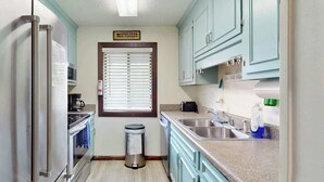 A compact kitchen with a stainless steel refrigerator, a built-in oven, a sink, and light blue cabinets. - Shipwatch Pointe II  P-302 (Myrtle Beach)