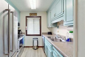 A compact kitchen with a stainless steel refrigerator, a built-in oven, a sink, and light blue cabinets. - Shipwatch Pointe II  P-302 (Myrtle Beach)